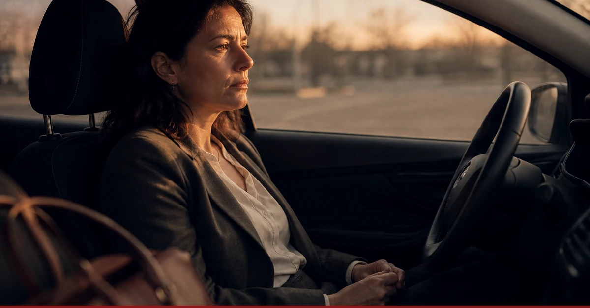 Eine Frau sitzt am frühen Abend im geparkten Auto, ohne loszufahren, die Hände im Schoß und den Blick durch die Windschutzscheibe: der Moment zwei Stunden nach einem Gespräch, das erledigt sein sollte.